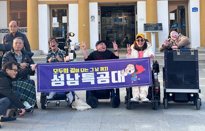 [수원=뉴시스] 지난 11월 경춘선 김유정역에서 성남특공대 회원들이 '모두의 길이 되는 그날까지! 성남특공대'라고 적힌 현수막을 들고 있다. 이들은 휠체어를 타고 직접 현장을 누비며 장애인 보행 환경 개선 활동을 펼치고 있다. (사진=성남시한마음복지관 제공) 2025.12.22. photo@newsis.com *재판매 및 DB 금지