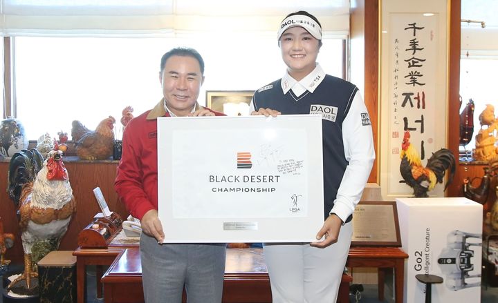 [서울=뉴시스] 제너시스BBQ 그룹이 후원하는 LPGA 투어 프로골퍼 유해란 선수가 지난해 우승한 블랙데저트 대회 당시 우승 홀 깃발에 사인과 다짐을 적어 윤홍근 회장에게 전달하고 있다. (사진=제너시스BBQ 그룹 제공) 2026.01.07. photo@newsis.com *재판매 및 DB 금지