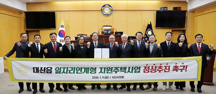 [서산=뉴시스] 충남 서산시의회 의원들이 9일 시의회 본회의장에서 대산읍 일자리연계형 지원주택사업 정상추진 촉구 결의문을 채택한 후 관련 현수막을 들고 기념 사진을 찍고 있다. (사진=서산시의회 제공) 2026.01.09. photo@newsis.com *재판매 및 DB 금지