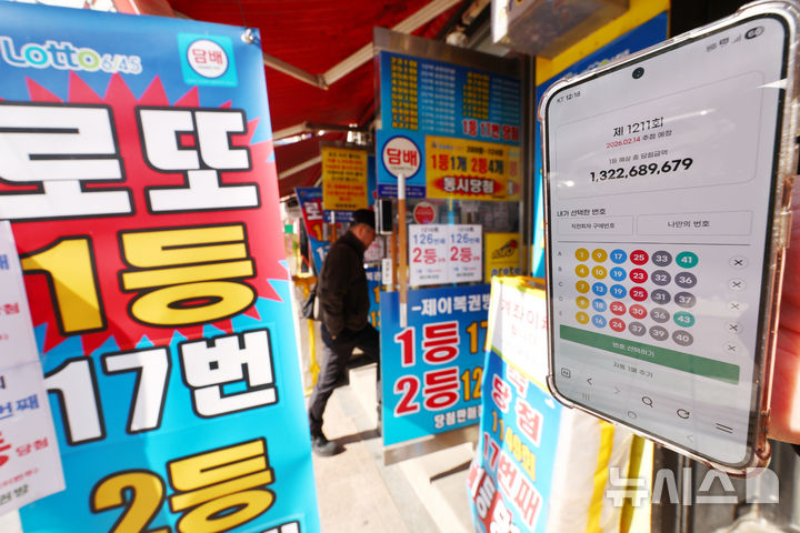 [서울=뉴시스] 김명년 기자 = 9일 오전 서울 시내 한 복권 판매점 앞에서 휴대폰 화면에 나오는 로또 모바일 판매 페이지 뒤로 시민들이 로또를 구매하고 있다. 2026.02.09. kmn@newsis.com
