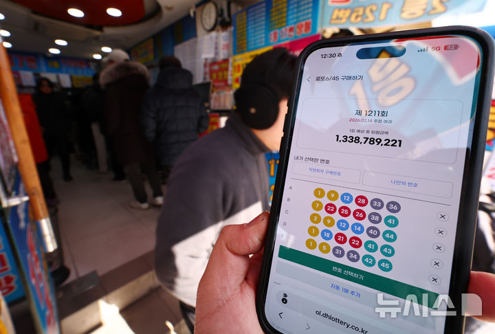 [서울=뉴시스] 김명년 기자 = 24년 만에 모바일 로또 판매가 시작된 9일 오전 서울 시내 한 복권 판매점 앞에서 휴대폰 화면에 나오는 로또 모바일 판매 페이지 뒤로 시민들이 로또를 구매하고 있다. 이용자는 모바일 동행복권 홈페이지에 가입한 뒤 예치금을 충전하면 오전 6시부터 자정까지 복권을 살 수 있다. 올해 상반기에는 평일에만 회차당 1인 5000원까지 살 수 있으며, PC 온라인 구매 금액과 합산해 계산된다. 토요일에는 모바일 구매가 막힌다. 전체 온라인 판매 규모도 전년도 로또 판매액의 5% 이내로 묶여, 한도에 도달하면 판매가 자동 중단된다. 2026.02.09. kmn@newsis.com