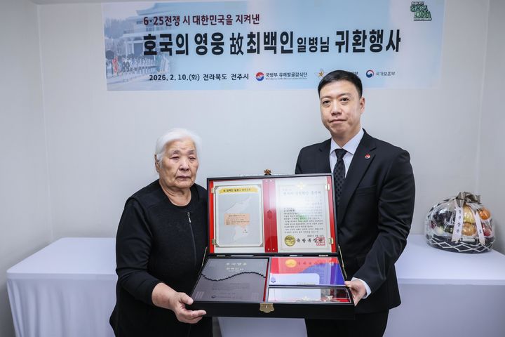 [서울=뉴시스] 김성환 국방부 유해발굴감식단장 직무대리가 10일 전북 전주에서 열린 호국영웅 고(故) 최백인 일병 귀환행사에서 고인의 여동생 최길자 씨에게 전사자 신원확인 통지서 등이 담긴 호국의 얼 함을 전달하고 있다. (사진=국방부유해발굴감식단 제공) 2026.02.10. photo@newsis.com *재판매 및 DB 금지