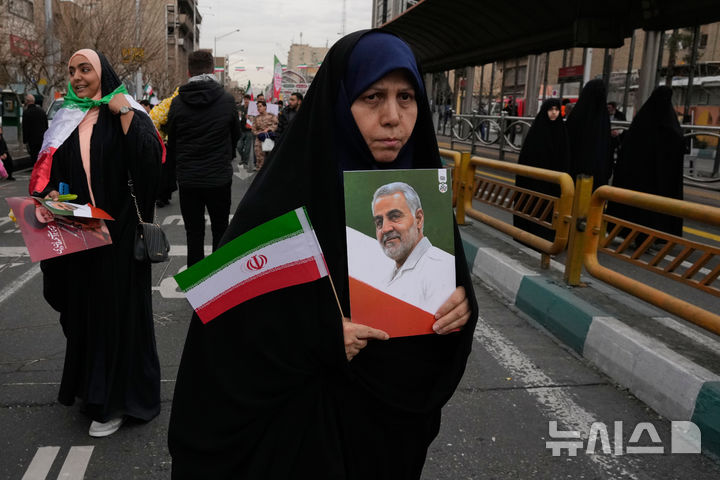  [테헤란=AP/뉴시스] 이란 이슬람 혁명 기념일인 11일 테헤란에서 한 여성이 이란 국기와 지난해 6월 이스파엘의 공습으로 숨진 혁명 수비대 장교의 사진을 들고 있다.2026.02.12.