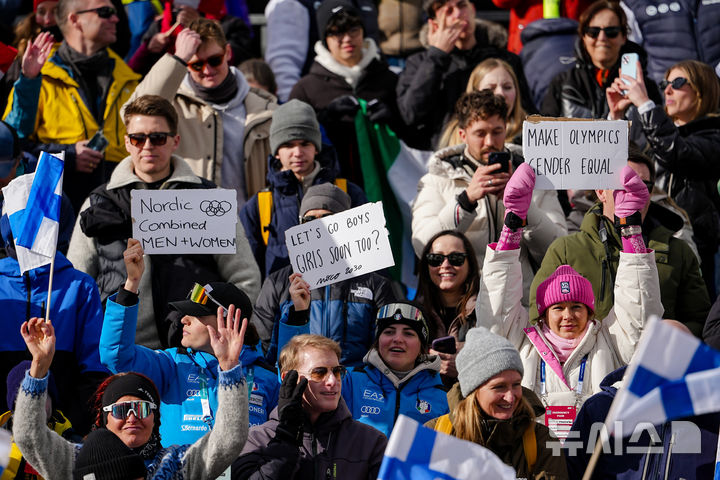 [테세로=AP/뉴시스] 미국의 노르딕복합 선수 아니카 말라친스키(오른쪽)가 17일(현지 시간) 이탈리아 테세로 크로스컨트리 스키 스타디움에서 열린 2026 밀라노·코르티나담페초 동계올림픽 노르딕복합 개인 군데르센 라지힐(10㎞) 경기장을 찾아 여성 노르딕복합 선수의 올림픽 출전 허가를 요구하는 팻말을 들고 있다. 2026.02.18.