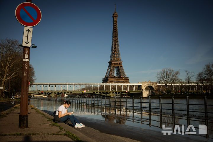 A woman reads on the flooded banks of the Seine next to the Eiffel Tower in Paris, Wednesday Feb. 25. 2026. (AP Photo/Thomas Padilla)