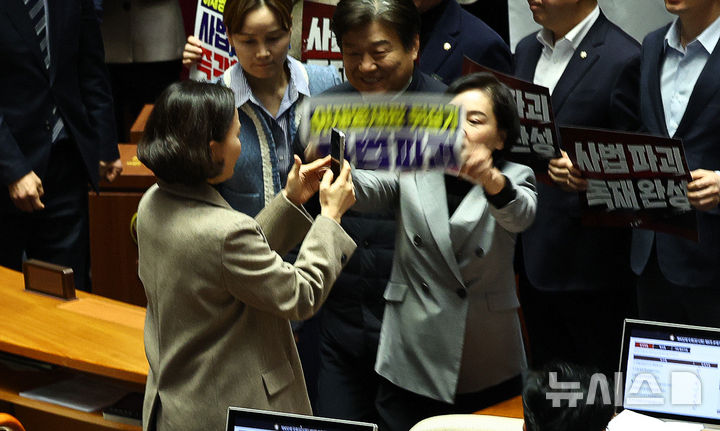 [서울=뉴시스] 김명년 기자 = 서명옥 국민의힘 의원이 27일 오후 서울 여의도 국회 본회의에서 '사법개혁 3법 반대' 관련 구호가 적힌 현수막과 피켓을 들고 항의 하던 도중 이를 촬영하는 이해민 조국혁신당 의원의 핸드폰을 피켓으로 내리치려 하고 있다. 2026.02.27. kmn@newsis.com