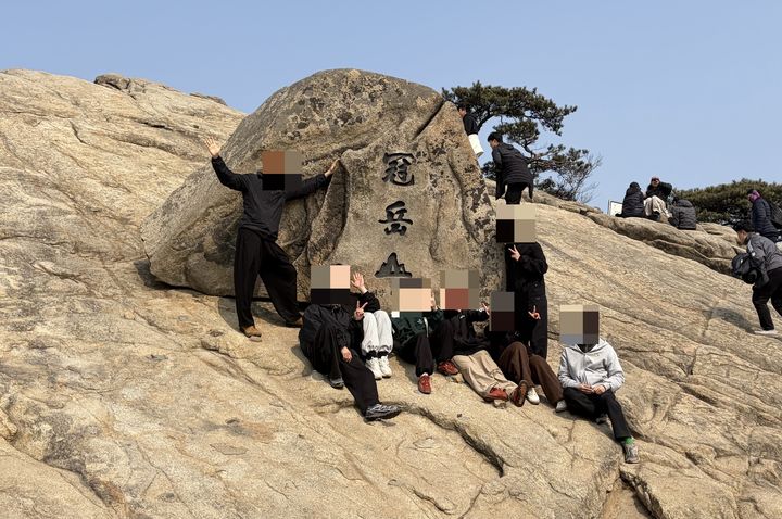 [서울=뉴시스] 김건민 인턴기자 = 젊은 등산객들이 관악산 정상에 위치한 비석 앞에서 단체 사진을 찍고 있다. 비석에는 '관악산'이라는 한자가 새겨져 있다. 2026.03.11. *재판매 및 DB 금지