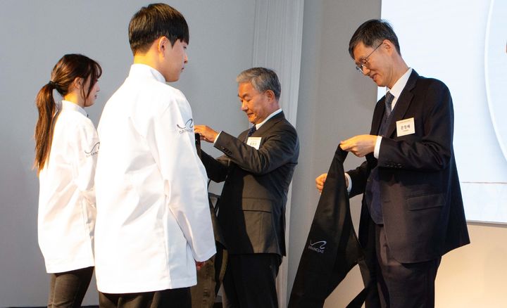 [서울=뉴시스] 지난 10일 평창 바랑재에서 진행된 바랑재드림키친 입학식에 문형배 전 헌법재판소 재판관과 홍봉성 라이나전성기재단 이사장이 참석해 참가 청년들에게 앞치마를 수여하고 있다. (사진=라이나생명 제공) 2026.03.12. photo@newsis.com *재판매 및 DB 금지