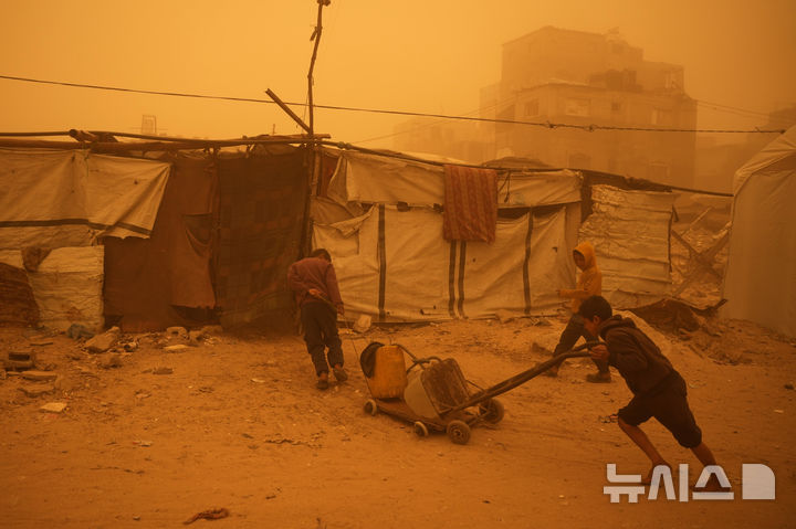 [AP/뉴시스] 14일 가자 지구 남부 칸유니스에 모래폭풍이 불어치는 가운데 아이들이 물이 든 플라스틱 통을 끌고 있다