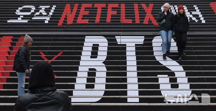 [서울=뉴시스] 추상철 기자 = 방탄소년단(BTS)의 서울 광화문광장 컴백 공연을 엿새 앞둔 15일 오후 서울 종로구 세종문화회관 계단에서 외국인관광객이 BTS 컴백 공연 관련 래핑 광고를 배경으로 기념촬영을 하고 있다. 2026.03.15. scchoo@newsis.com