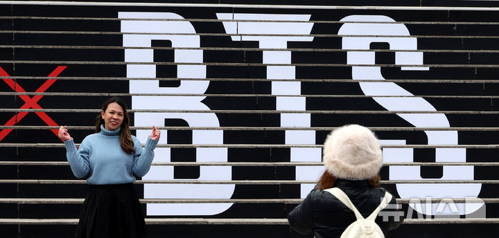 [서울=뉴시스] 추상철 기자 = 방탄소년단(BTS)의 서울 광화문광장 컴백 공연을 엿새 앞둔 15일 오후 서울 종로구 세종문화회관 계단에서 외국인관광객이 BTS 컴백 공연 관련 래핑 광고를 배경으로 기념촬영을 하고 있다. 2026.03.15. scchoo@newsis.com