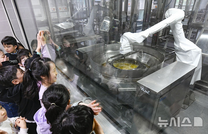 [수원=뉴시스] 김종택 기자 = 18일 경기 수원시 대평초등학교 거점형 학교급식 튀김 지원실에서 1학년 학생들이 음식을 조리하는 급식 로봇을 살펴보고 있다.&nbsp; 전국 최초로 대평초에 설치된 거점형 학교급식 튀김 지원실은 최첨단 튀김 로봇을 도입해 공동으로 조리한 뒤 인근 학교에 제공하는 새로운 학교 급식 모델이다. (공동취재) 2026.03.18. photo@newsis.com