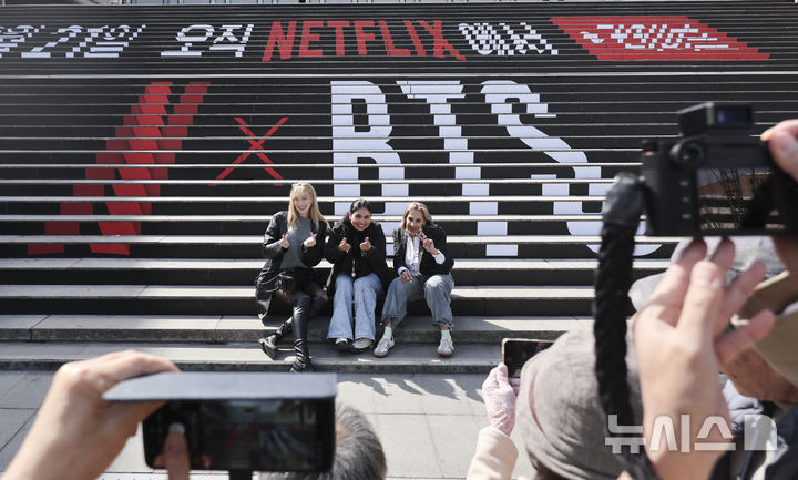 [서울=뉴시스] 황준선 기자 = BTS(방탄소년단)의 광화문광장 컴백 공연을 이틀 앞둔 지난 19일 서울 종로구 세종문화회관 계단에 설치된 홍보물 앞에서 외국인들이 기념촬영을 하고 있다. 2026.03.20. hwang@newsis.com