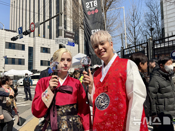 [서울=뉴시스] 한이재 기자 = 21일 방탄소년단 복귀 공연을 보기 위해 직접 만든 붉은색 한복을 입고 온 김택호(36)씨와 안나(23)씨가 응원봉을 들어 보이고 있다. 2026.03.21. nowone@newsis.com