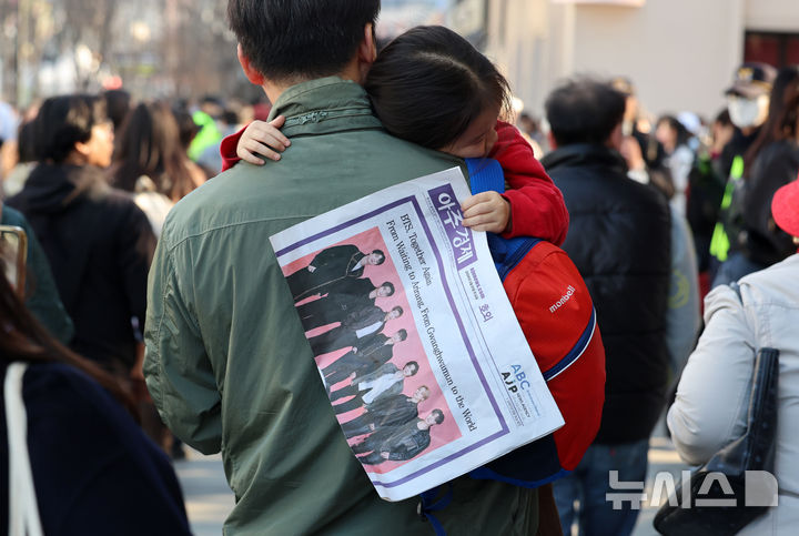 [서울=뉴시스] 조성우 기자 = 방탄소년단(BTS) 컴백 공연 당일인 21일 서울 종로구 광화문광장에서 아버지 품에 안긴 이아가 BTS 공연 기념 호외를 들고 가고 있다. 2026.03.21. xconfind@newsis.com