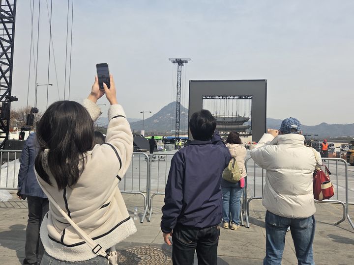 [서울=뉴시스] 이지영 기자= 22일 광화문 광장 인근에는 전날 공연을 보지 못한 아쉬움에 머무르는 팬들과 관광객들로 북적였다. 철거 작업 중인 빈 무대라도 함께 찍겠다며 무대 200m 지점 앞에서 사진을 찍는 모습도 이어졌다. 2026.03.22. jee0@newsis.com *재판매 및 DB 금지