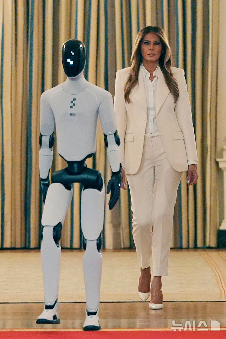 [워싱턴=AP/뉴시스] 도널드 트럼프 미국 대통령 부인 멜라니아 여사가 25일(현지 시간) 백악관에서 열린 ‘함께 미래 키우기' 글로벌 정상회의에 참석해 미국 제조 휴머노이드 로봇 '피겨3'과 함께 입장하고 있다. 2026.03.26.