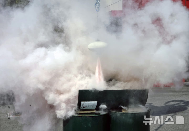 [완주=뉴시스] 26일 전북 완주군 구이면 구이119안전센터 앞에서 진행된 자동확산소화기 시연 현장에서 크레인에 매달린 자동확산소화기가 불길을 감지하자 소화약제를 내뿜고 있다. 2026.03.26. lukekang@newsis.com