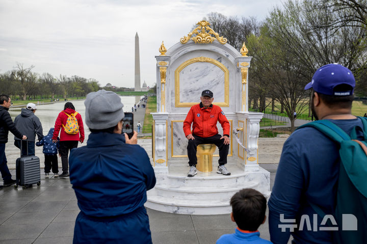 [워싱턴=AP/뉴시스] 30일(현지 시간) 미국 워싱턴DC 내셔널 몰에서 방문객이 ‘왕에게 어울리는 왕좌'(A throne fit for a king)라는 제목의 황금 변기에 앉아 기념 촬영을 하고 있다. 이 변기는 게릴라 예술그룹 '시크릿 핸드셰이크'라는 단체가 만든 것으로 백악관 리모델링에 집착하는 도널드 트럼프 대통령을 조롱하는 작품이다. 2026.03.31.