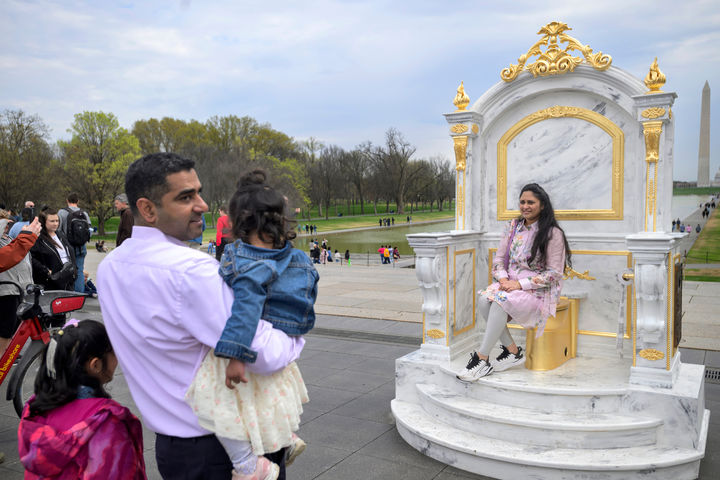 [워싱턴=AP/뉴시스] 30일(현지 시간) 미국 워싱턴DC 내셔널 몰에서 방문객들이 ‘왕에게 어울리는 왕좌'(A throne fit for a king)라는 제목의 황금 변기에 앉아 기념 촬영을 하고 있다. 이 변기는 게릴라 예술그룹 '시크릿 핸드셰이크'라는 단체가 만든 것으로 백악관 리모델링에 집착하는 도널드 트럼프 대통령을 조롱하는 작품이다. 2026.03.31.