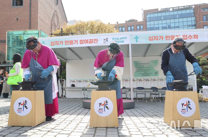 [서울=뉴시스] 이경상 주교, 정순택 대주교, 박용만 이사장(왼쪽부터)이 4월 12일 명동대성당에서 열린 ‘철조망 십자가 프로젝트’ 개막식에서 철조망을 두드려 펴는 시연을 하고 있다. (사진=천주교 서울대교구 제공) 2026.04.13. photo@newsis.com