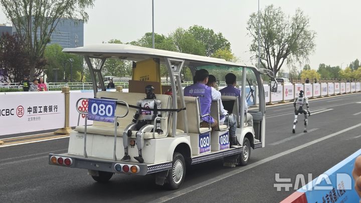 [베이징=뉴시스]박정규 특파원 = 19일 중국 베이징 이좡에서 열린 하프마라톤에서 대회 참가팀 차량이 뒷좌석에 휴머노이드 로봇을 태운 채 달리는 로봇을 쫓아가고 있다. 2026.04.19. pjk76@newsis.com