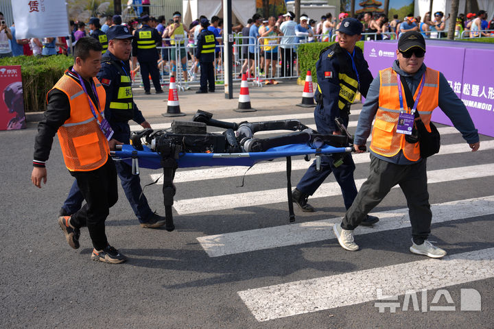 [베이징=AP/뉴시스] 19일(현지시간) 베이징 이좡(E-Town)에서 열린 '제2회 휴머노이드 로봇 하프마라톤 대회'에서 경기를 마친 로봇을 보안 요원과 참가자들이 들것에 실어 나르고 있다. 2026.04.19.