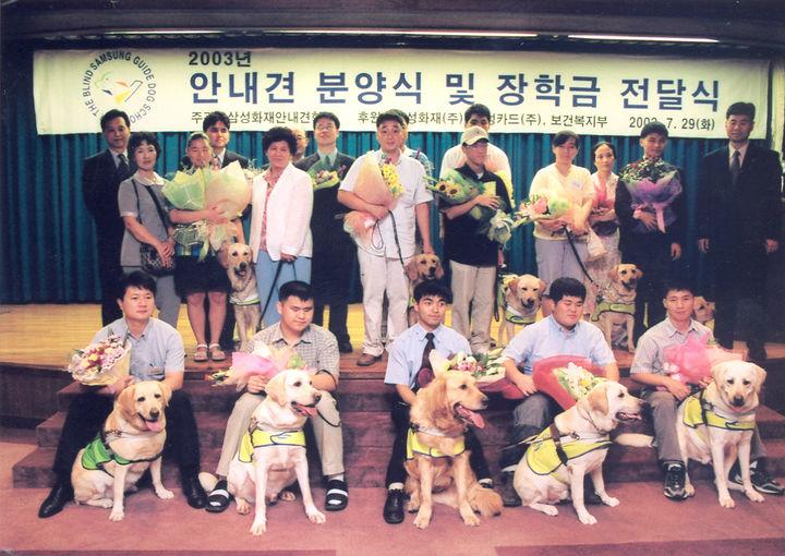 [세종=뉴시스](사진 아래 맨오른쪽)유석종 삼성화재 안내견학교 프로가 2003년 당시 삼성화재 안내견학교의 안내견 분양식에서 사진촬영을 하고 있다. (사진=유석종씨 제공) 2026.04.26. photo@newsis.com *재판매 및 DB 금지