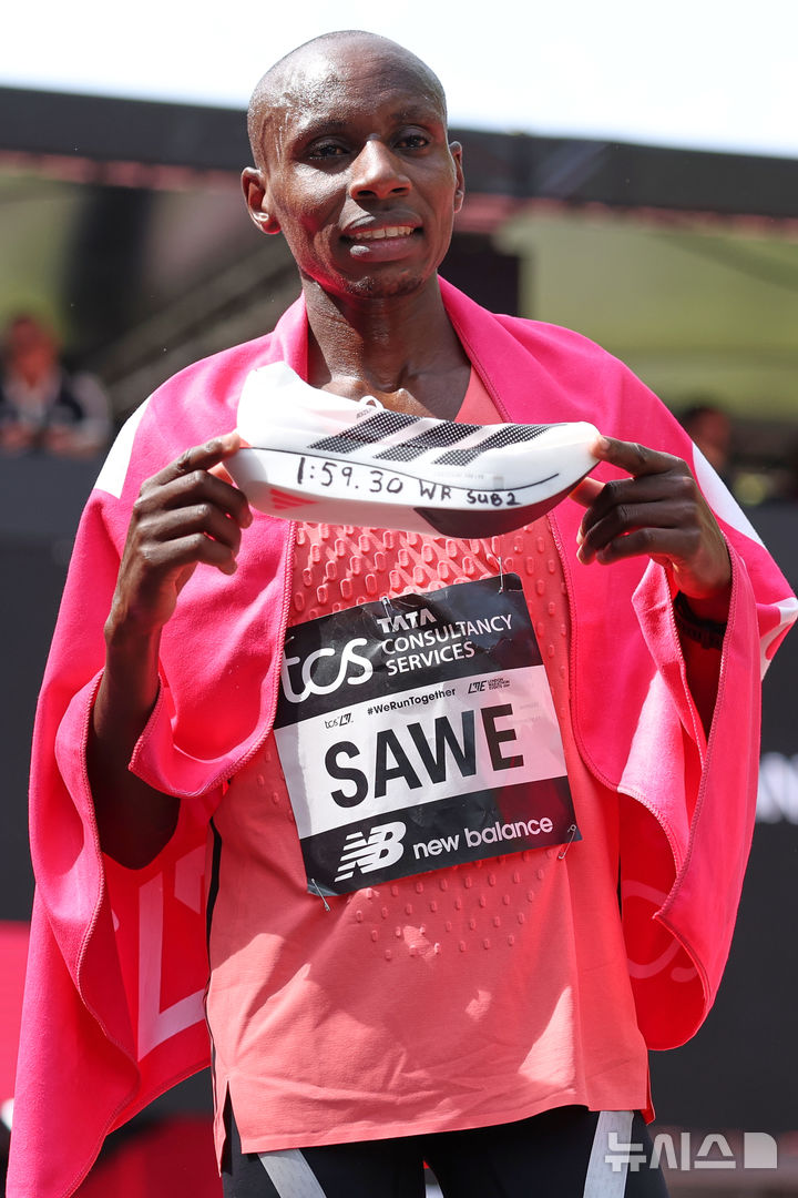 [런던=AP/뉴시스] 사바스티안 사웨(케냐)가 26일(현지 시간) 영국 런던에서 열린 2026 런던마라톤에서 1시간 59분 30초 세계신기록으로 결승선을 통과한 뒤 기록이 적힌 신발을 들고 포즈를 취하고 있다. 2026.04.26.