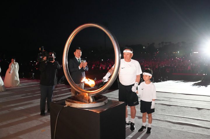 [제주=뉴시스] 8일 오후 서귀포시 공천포전지훈련센터 주경기장에서 제60회 제주도민체육대회 개막식이 열린 가운데 1966년 제1회 도민체전 성화 주자였던 고대오(75)씨와 김로은(중문초 1) 학생이 함께 성화를 점화하고 있다. (사진=제주도 제공) 2026.05.08. photo@newsis.com *재판매 및 DB 금지