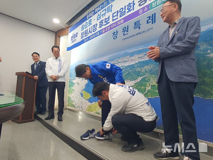 [창원=뉴시스] 강경국 기자 = 더불어민주당 송순호 경남 창원시장 후보와 심규탁 조국혁신당 창원시장 후보가 11일 창원시청 프레스센터에서 후보 단일화 선언 기자회견을 가진 후 운동화를 신겨 주는 퍼포먼스를 하고 있다. 2026.05.11. kgkang@newsis.com