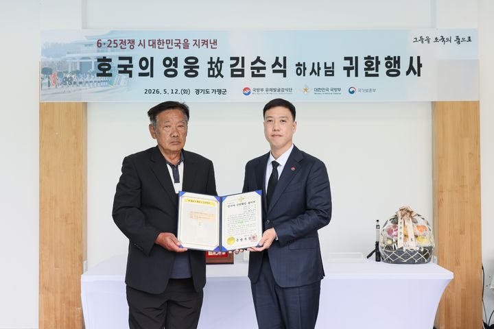 [서울=뉴시스] 12일 오전에 열린 '故 김순식 하사 호국의 영웅 귀환 행사'에서 김성환 국방부 유해발굴감식단장 직무대리(육군 중령, 오른쪽)가 고 김순식 하사의 아들 김의영 씨(72)에게 전사자 신원확인 통지서를 전달하고 있다. (사진=국방부 제공) 2026.05.12. photo@newsis.com *재판매 및 DB 금지