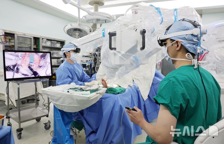 [서울=뉴시스] 권진근 서울아산병원 성형외과 교수(오른쪽)가 초미세수술 로봇을 이용해 하지 림프부종 환자에게 0.4㎜ 정도의 가느다란 림프관을 정맥에 연결하는 림프정맥간 문합술을 시행하고 있다. (사진= 서울아산병원 제공) 