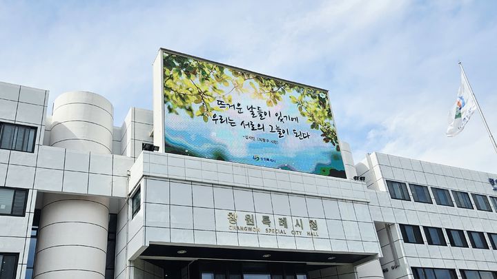 [창원=뉴시스] 강경국 기자 = 경남 창원시가 우리말 공감 글귀 '여름편' 문안으로 선정한 '뜨거운 날들이 있기에 우리는 서로의 그늘이 된다'가 시청 전광판에 노출되고 있다. (사진=창원시청 제공). 2026.05.21. photo@newsis.com *재판매 및 DB 금지