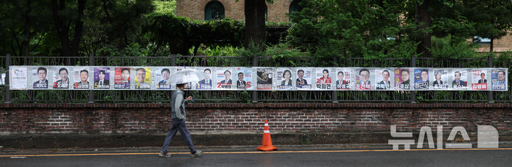 [서울=뉴시스] 전신 기자 = 21일 서울 종로구 예술가의 집 담장에 부착된 제9회 전국동시지방선거 선거벽보 앞을 한 시민이 지나고 있다. 2026.05.21. photo1006@newsis.com
