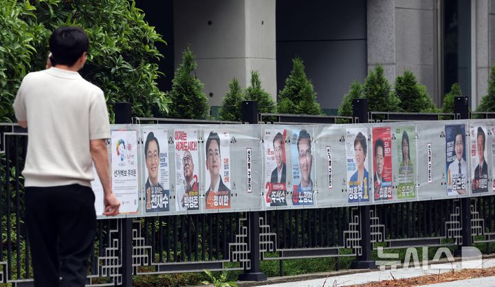  [부산=뉴시스] 하경민 기자 = 21일 부산 연제구의 한 거리에서 시민이 담장에 부착된 선거벽보를 보고 있다.&nbsp; 부산시선거관리위원회는 제9회 전국동시지방선거와 국회의원 부산 북구갑 보궐선거 후보자의 선거벽보를 부산 내 1750여 곳에 부착한다. 2026.05.21. yulnetphoto@newsis.com
