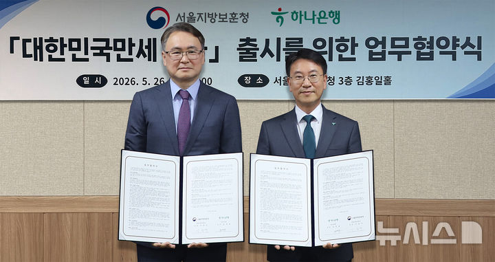 [서울=뉴시스]하나은행은 지난 26일 오후 서울 용산구 서울지방보훈청에서 호국보훈의 달을 맞아 '대한민국만세 적금' 출시를 위한 업무협약을 체결했다. 이날 협약식에 참석한 김영호 하나은행 리테일그룹 그룹장(사진 오른쪽)이 이승우 서울보훈청장(사진 왼쪽)과 함께 협약서를 들고 기념촬영을 하고 있다. (사진=하나은행 제공). 2026.05.28. photo@newsis.com 
