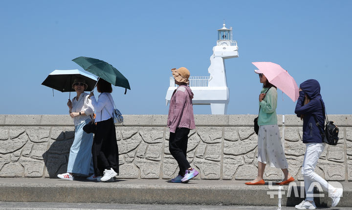 [제주=뉴시스] 우장호 기자 = 낮 기온이 오르며 제법 더운 날씨를 보인 지난달 31일 오전 제주시 이호포구 말등대에서 양산을 쓴 외국인 관광객들이 지나가고 있다. 2026.05.31. woo1223@newsis.com