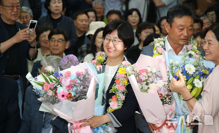 [제주=뉴시스] 우장호 기자 = 고의숙 제주도교육감 후보가 3일 제주시 삼도1동에 위치한 선거사무소에서 당선이 확실시 되자 남편 강경식씨와 함께 꽃다발을 목에 걸고 환호하고 있다. 2026.06.03. woo1223@newsis.com
