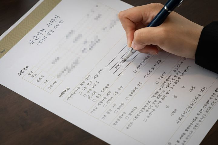 [서울=뉴시스] 사랑의열매 최연소 유산기부자인 30대 초반 여성 A씨가 유산기부 서약서에 기부 자산으로 사망보험금을 기재하고 있는 모습 (사진=사랑의열매 제공) 2026.06.11. photo@newsis.com *재판매 및 DB 금지