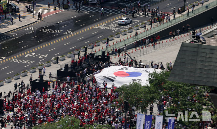 [서울=뉴시스] 조수정 기자 = 12일 오전 서울 종로구 광화문광장에서 시민들이 2026 FIFA 북중미 월드컵 조별리그 대한민국-체코 경기 관전 및 응원을 위해 모여 대형 태극기를 들어올리고 있다. 응원하는 시민들 위 KT 광화문빌딩 웨스트 대형 미디어월에는 KT와 국내 공식 월드컵 중계사인 JTBC가 협력해 경기 영상이 생중계된다. 2026.06.12. chocrystal@newsis.com