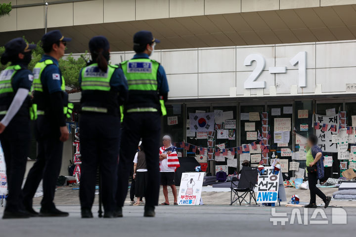 [서울=뉴시스] 조성우 기자 = 18일 오후 6.3 지방선거 투표용지 부족 사태를 규탄하는 시위가 14일째 열리고 있는 서울 송파구 올림픽공원 핸드볼경기장 앞에서 시위 참가자들이 출입문을 지키는 가운데 경찰이 인근에서 경계 근무를 서고 있다. 2026.06.18. xconfind@newsis.com