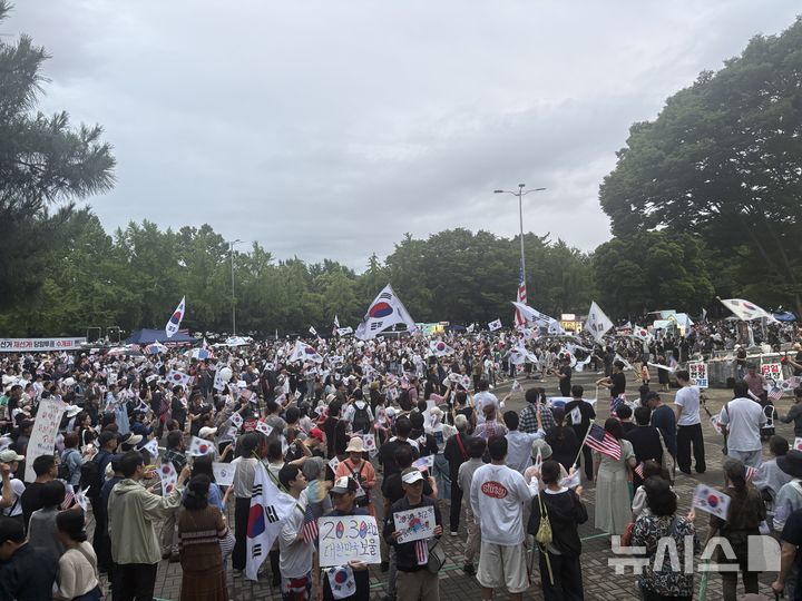 [서울=뉴시스]최은수 기자=20일 오후 서울 송파구 올림픽공원 핸드볼경기장 앞에서 6·3 지방선거 투표용지 부족 사태에 항의하는 '개표소 봉쇄 시위'가 16일째 이어지고 있다. 비가 오락가락하는 날씨 속에서도 참가자들이 태극기와 성조기를 흔들며 재선거와 당일투표 수개표를 요구하고 있다. 2026.06.20. eschoi@newsis.com