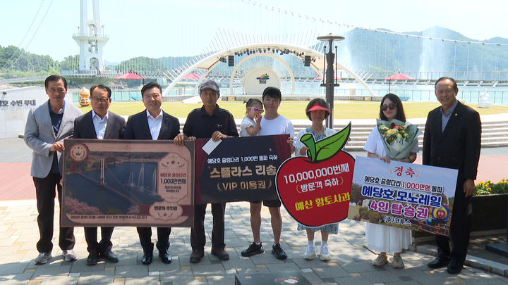 [예산=뉴시스] 29일 충남 예산 예당호 출렁다리를 찾은 1000만번째 관광객 김건호씨 가족이 군 관계자 등과 출렁다리를 배경으로 기념 사진을 찍고 있다. (사진=예산군 제공) 2026.06.29. photo@newsis.com *재판매 및 DB 금지