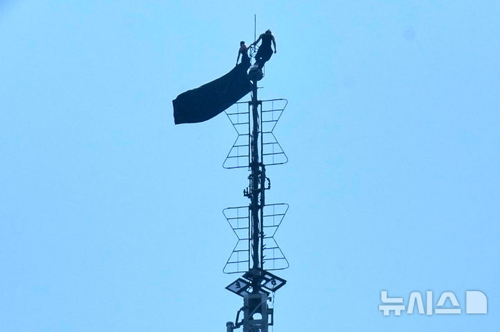 [뉴욕=AP/뉴시스] 러시아 출신 고공 스턴트 커플인 안젤라 니콜라우와 이반 비어쿠스 1일(현지 시간) 미국 뉴욕 엠파이어 스테이트빌딩 꼭대기에서 현수막을 펼쳐 보이고 있다. 2026.07.02.