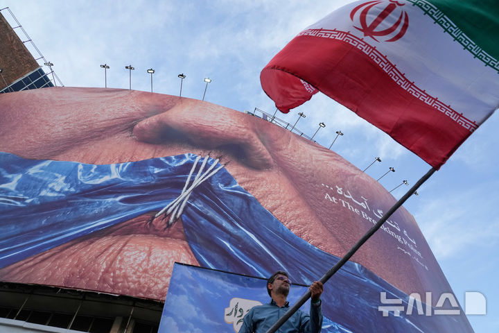 [테헤란=AP/뉴시스] 이란 정부가 자국 정예군인 이슬람혁명수비대(IRGC)를 국가안보 위협 단체로 지정하려는 영국 정부의 움직임에 반발해 주이란 영국대사를 초치했다. 16일(현지시간) AP통신 등에 따르면 이란 외무부는 전날 휴고 쇼터 주이란 영국대사를 불러 영국의 IRGC 지정 추진에 강력히 항의했다. 사진은 지난 5월6일(현지시간) 이란 수도 테헤란 도심 광장에서 한 남성이 친정부 캠페인의 하나로 이란 국기를 흔들고 있는 모습. 뒤편 전광판에는 호르무즈 해협과 입이 꿰매진 도널드 트럼프 미국 대통령을 묘사한 그림이 표시돼 있다. 2026.07.16.