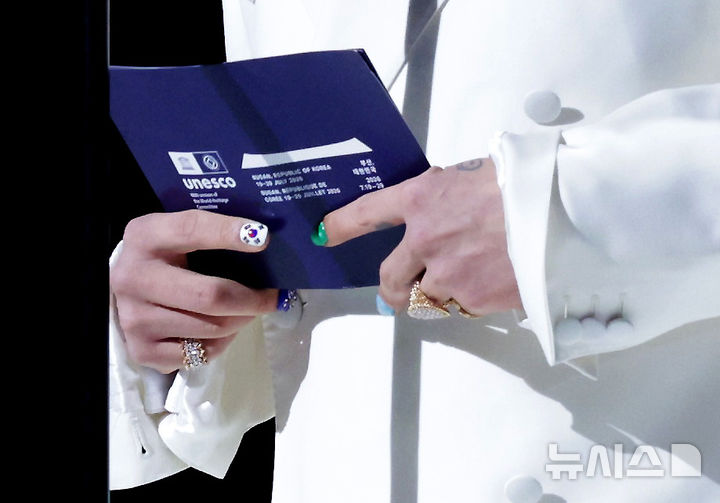 [부산=뉴시스] 김진아 기자 = 가수 지드래곤(GD·권지용)이 19일 부산에서 열린 제48차 유네스코 세계유산위원회 개회식에서 메시지 퍼포먼스를 하고 있다. 흰색 정장에 파란색 행커치프를 장식한 지드래곤의 오른손 검지에는 태극기 네일아트가 그려져 있다. 2026.07.19. bluesoda@newsis.com