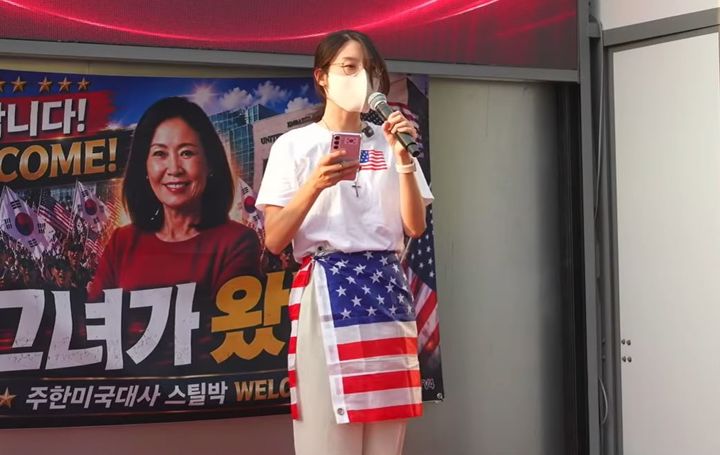 [서울=뉴시스] 성조기를 두른 30대 여성 A씨가 미셸 스틸 신임 주한미국대사 환영 집회에서 한미동맹과 안보 현안에 대한 입장을 밝혔다. (사진='황교안 TV' 유튜브 채널 캡처)