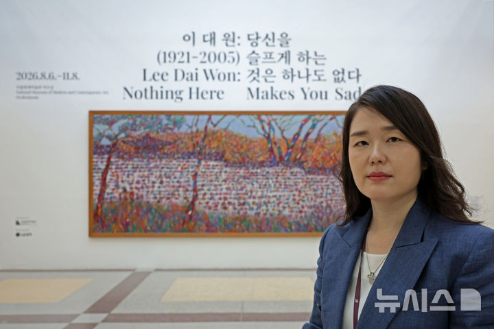 [서울=뉴시스] 박진희 기자 = 이대원 회고전 입구에 공개된 '담'에서 선 배원정 학예연구사. 가로 5m의 이 작품은 미국 주재 한국대사관 소장품으 이번 전시를 위해 대여했다. 2026.08.05. pak7130@newsis.com2026.08.05. pak7130@newsis.com
