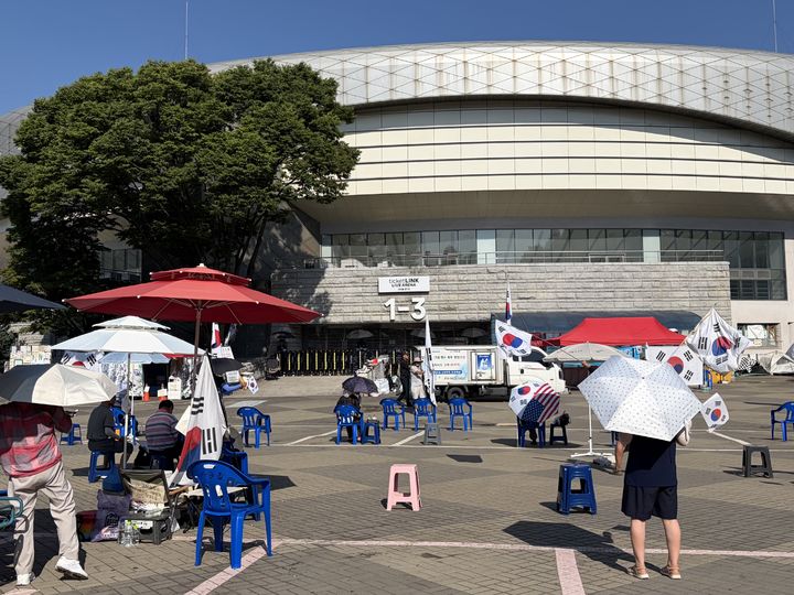 [서울=뉴시스] 김서하 인턴기자 = 연일 폭염이 계속되는 가운데 투표용지 부족 사태에 항의하는 개표소 봉쇄 시위가 64일째 이어지고 있는 7일 오전 서울 송파구 올림픽공원 핸드볼경기장 앞에서 참가자들이 태극기와 성조기를 흔들고 있다. 2026.08.07. photo@newsis.com *재판매 및 DB 금지